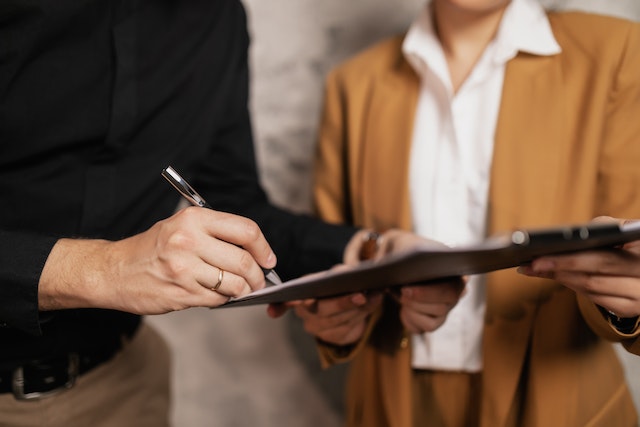 someone signing a document on a clipboard while someone else oversees the process